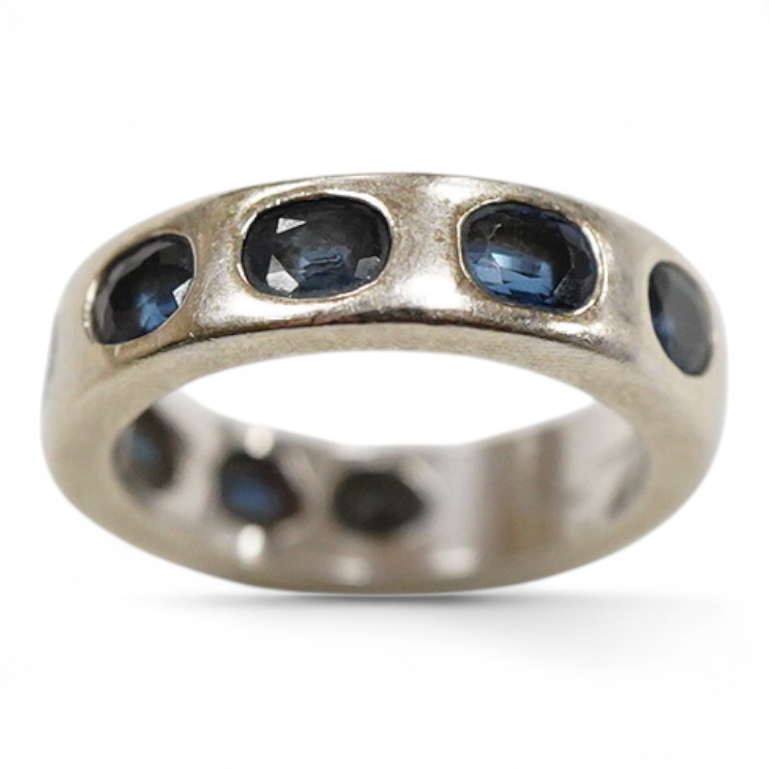 A recent Italian white metal (stamped 750) and seven stone gypsy set oval cut sapphire band, by Cristiano of Genoa, size N, gross weight 10.4 grams.